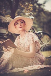 Blond beautiful retro woman reading book on a meadow